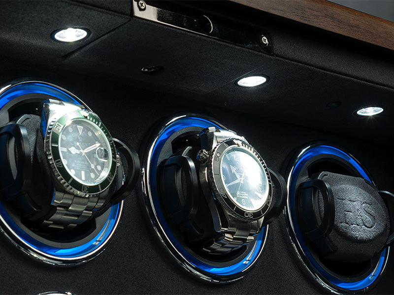 Three watches in a display case with blue accents on a dark background